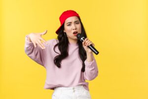 Suonare Con La Voce: Ecco Il Beatboxing 5 People Emotions Lifestyle Leisure And Beauty Concept Stylish And Cool Young Girl Rapper In Red Cap Singing Song And Gesturing Performing With Microphone Standing Yellow Background 1