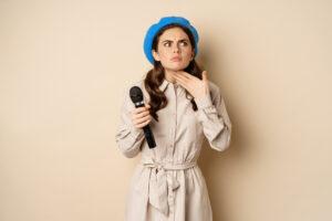 Migliorare La Voce: Tecniche Di Riscaldamento E Allenamento Vocale 8 Cantante Alla Moda Donna Con Microfono Che Tocca La Gola Si Sente Male In Piedi Su Sfondo Beige Copia Spazio 1