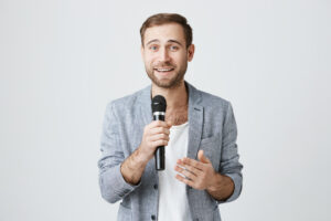 Public Speaking E Crescita Personale: Sblocca Il Tuo Potenziale Con La Voce 7 Bel Giovane Intrattenitore Con Microfono Dando Il Discorso 1